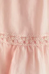 Blusa rosada de tejido liviano con alforzas e inserciones de encaje, escote en V pronunciado, cierre frontal de botones y mangas mariposa cortas con terminación fruncida en el ruedo.