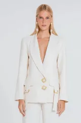 Blazer color marfil de corte estructurado, con solapas clásicas, cierre frontal de dos botones decorativos con detalle de piedra y bolsillos con solapa y correas laterales ajustables.