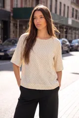 Blusa cruda con estampado de lunares negros, de manga corta y cuello redondo.