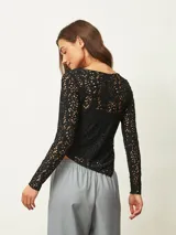 Top de encaje negro con diseño calado, manga larga y cuello redondo. Presenta un corte ajustado y un ruedo asimétrico.