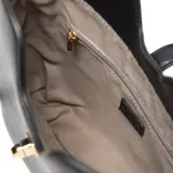 Cartera estructurada mediana de cuero sintético negro, con asa corta fija y correa larga regulable y desmontable. Presenta un broche giratorio metálico en el cierre superior y un detalle de herraje metálico dorado en el frente, con el logo XL aplicado.