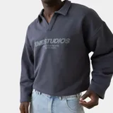 Polo crewneck de EmeStudios en color azul marino, con cuello tipo polo sin botones y mangas largas de caída amplia. Presenta el logo de la marca y un mensaje bordado en el frente en tono sobre tono.
