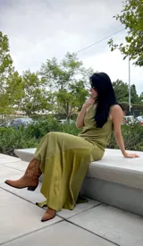 Vestido largo de corte recto y sin mangas, con cuello alto y una abertura lateral pronunciada en la falda. Presenta una textura suave tipo gamuza en color verde oliva.