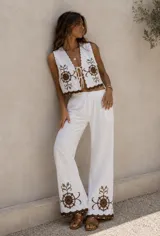 Conjunto de dos piezas color blanco con bordados marrones, compuesto por un chaleco corto con escote en V y lazos frontales, y un pantalón largo de corte ancho con cintura elástica.