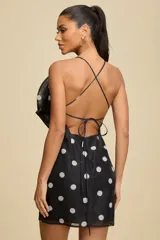 Vestido corto negro con estampado de lunares blancos, presenta un diseño de escote halter con una gran aplicación floral tridimensional en el pecho.