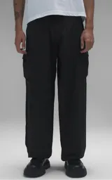 Pantalón estilo técnico de corte oversize, color negro, confeccionado en textil memory. Presenta diseño funcional con cinco bolsillos, incluyendo dos bolsillos cargo laterales de gran tamaño, y cuenta con un cinturón regulable integrado con hebilla de encastre.