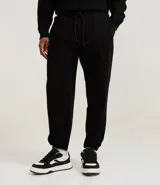 Pantalón jogger negro de algodón y poliéster, con cintura elástica y cordón ajustable. Presenta bolsillos laterales y puños ajustados en los tobillos.