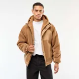 Campera con capucha color beige, con efecto borreguito en el cuerpo y las mangas, y detalles en tela lisa beige en los hombros y el pecho. Tiene cierre frontal y botones a presión.