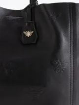 Cartera tipo shopper Jazmin Chebar modelo Honey, color negro, confeccionada en cuero vacuno suave. Cuenta con amplia capacidad, doble asa larga para el hombro y diseño grabado con abejas en bajo relieve. Incluye un tag colgante decorativo con dije metálico en forma de abeja.