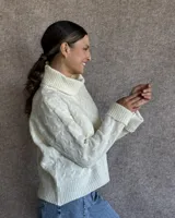 Sweater de lana color crudo con cuello alto y diseño trenzado.