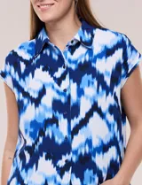 Túnica de gasa negra con estampado floral en tonos azules y blancos, cuello camisero, manga corta y cierre frontal de botones.
