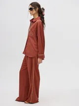 Pantalón de corte holgado y tiro alto con caída recta, color azul petróleo. Presenta una franja lateral decorativa en tonos rojo y amarillo que recorre la pierna, a juego con la camisa de la misma línea.