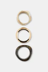 Pack de tres pulseras rígidas de diferentes formas y tamaños: una en tono marfil jaspeado, una dorada metálica brillante y otra oscura efecto carey.