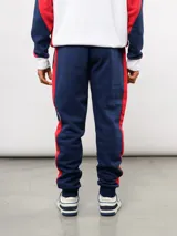 Pantalon de jogging azul de felpa, con franjas laterales en blanco y azul marino. Presenta el escudo del Club Nacional de Football en el muslo derecho y el logo de Umbro en el izquierdo.