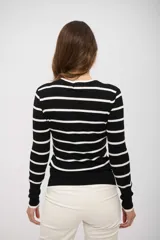 Suéter de punto ajustado, color negro con rayas horizontales blancas. Presenta cuello redondo y mangas largas con puños ajustados.