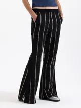 Pantalón negro de tiro alto con fit flare, confeccionado en jacquard con motivo de cadenas doradas que forman rayas verticales. Presenta tajos en los laterales del ruedo.