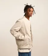 Campera bomber color beige, con cuello alto, cierre frontal con cremallera, bolsillos laterales y puños y cintura elastizados.