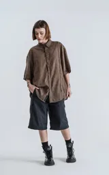 Camisa de corte oversize y mangas cortas, confeccionada en tejido con efecto desgastado color marrón chocolate. Presenta cuello clásico, cierre frontal con botones y diseño holgado.
