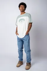 Remera de corte holgado con diseño color block, combinando paneles en color verde menta y blanco. Presenta un estampado frontal con la palabra 'Lucky' dentro de un óvalo y dibujos de flores con lentes de sol.