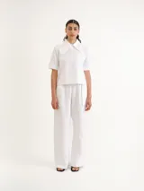 Camisa blanca de manga corta con cuello camisero grande y marcado, cierre frontal oculto y bolsillo ojal en el pecho.