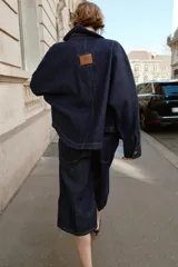 Cazadora de denim azul oscuro con cuello solapa, manga larga, cierre frontal con botones metálicos y bolsillos delanteros de plastrón.