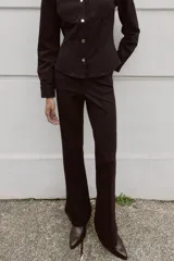 Pantalón flare de tiro bajo color marrón oscuro, con bolsillos delanteros y traseros, pierna entallada y bajo acampanado. Cierre frontal con cremallera y botón.