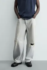 Jeans de mezclilla, tiro medio, color celeste claro lavado con efecto desgastado y roturas pronunciadas en ambas piernas. Corte ancho y relajado.