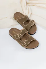 Sandalias de cuero color tostado con diseño de doble tira ajustable mediante hebillas metálicas. Presentan costuras decorativas en hilo blanco a lo largo de las tiras y una base anatómica de corcho con suela de goma.