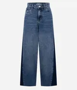 Pantalón de jean modelo wide leg con cintura media y cierre tradicional. Presenta un diseño bicolor con un recorte lateral en tono más oscuro que contrasta con el resto de la prenda, aportando una silueta alargada.