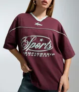 Remera de corte boxy color bordó, con cuello en V en color menta, mangas cortas con recortes y estampa frontal con temática deportiva en color menta.