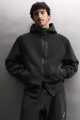 Sudadera con capucha de entrenamiento, confeccionada en tejido técnico de algodón con efecto neopreno. Presenta cierre frontal de cremallera, cuello subido, bolsillos laterales y un bolsillo en el pecho, todos con cierre de cremallera y acabado termofijado.