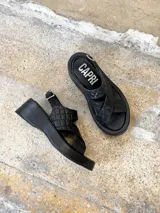 Sandalias negras de cuero con plataforma, tiras cruzadas y hebilla lateral.
