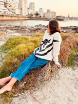 Sweater de lana color crema con cuello redondo, mangas largas y diseño con apliques de cuero negro en forma de V en el frente y bordado de una rosa negra en el pecho.