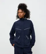 Campera rompevientos azul marino con cuello alto ajustable, cierre frontal y cordones en la cintura para un ajuste entallado. Presenta detalles de costuras en contraste blanco y puños elásticos.