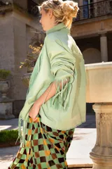 Chaqueta de cuero ovino color verde menta, con cuello sastre, cierre frontal de botones y flecos decorativos en las solapas, mangas y puños. Presenta un diseño holgado y bolsillos laterales.