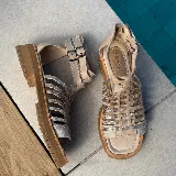 Sandalias bajas de cuero color beige con tiras horizontales plateadas y cierre con hebilla al tobillo.