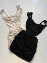 Vestido corto de tela fruncida, color gris claro, con escote corazón y tirantes finos anudados en los hombros. Presenta un efecto drapeado en todo el cuerpo.