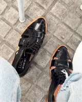 Zapato acordonado de cuero vacuno color marrón con aberturas laterales y cordones negros.