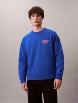 Buzo de felpa azul con cuello redondo, manga larga y corte regular. Presenta puños y dobladillo acanalados, con el logo y bordado 'Very' de Calvin Klein en el pecho.