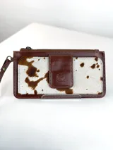 Billetera tipo porta celular de cuero, con diseño combinado en cuero liso marrón y cuero con pelo vacuno estampado. Cuenta con cierre superior, correa de muñeca y solapa frontal con cierre magnético y logo de búho grabado.