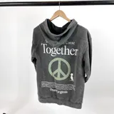 Canguro gris lavado de corte oversize con capucha y cordón ajustable. Estampa en la espalda con la frase "We Come Together" y un símbolo de la paz.