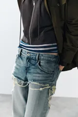 Jeans de tiro bajo y corte recto, color celeste con efecto lavado. Presenta diseño de doble tiro con detalle de short superpuesto con roturas, además de roturas adicionales en las perneras. Cuenta con cinco bolsillos, trabillas para cinturón y cierre frontal con cremallera y botón metálico.
