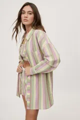 Camisa de corte oversize a rayas verticales en tonos verde, lila, marrón y amarillo, con cuello camisero, mangas largas y bolsillo aplicado en el frente.