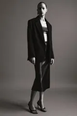 Falda midi de tiro medio, color negro, confeccionada en piel 100% con pespuntes marcados a tono y bajo recto. Cierre lateral con cremallera oculta en costura.