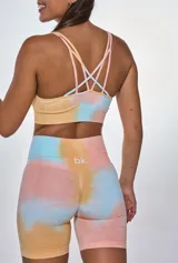 Conjunto deportivo compuesto por un top de escote redondo y un short de tiro alto, ambos con diseño tie-dye en tonos pastel salmón, amarillo y celeste. El top presenta el logo de la marca estampado en el frente.