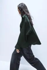 Camisa oversize de popelín de algodón, color verde oscuro, con cuello solapa, manga larga con puños abotonados y cierre frontal con botones.