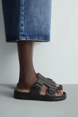 Sandalia tipo slide de goma, color verde militar, con dos tiras anchas ajustables mediante hebillas cuadradas. Presenta plantilla anatómica y suela gruesa con relieve.