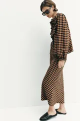 Falda midi de tiro alto con estampado de cuadros vichy en tonos marrón y negro. Presenta cintura elástica y un cinturón fino a contraste con hebilla metálica.