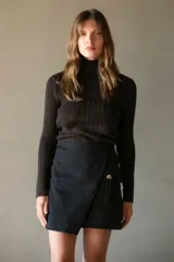 Falda corta negra de gabardina elastizada, con diseño cruzado tipo wrap y un bolsillo lateral con botón dorado.
