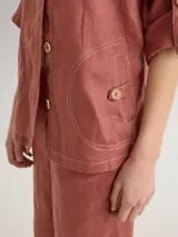 Chaqueta de lino color azul lavanda, de corte holgado, con escote redondo, cierre frontal con botones y mangas ajustables. Presenta un diseño versátil con bordado en la espalda.